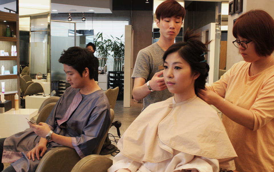 In this July 30, 2013 photo, Chinese couple Yang Candi, bottom right, and her fiance Chen Jingjing, bottom left, of Beijing sit in a salon chair in southern Seoul, South Korea, as two stylists put finishing touches on her hair. China is the source of one quarter of all tourists to South Korea, and a handful of companies in South Korea’s $15 billion wedding industry are wooing an image-conscious slice of the Chinese jet set happy to drop several thousand dollars on a wedding album with a South Korean touch. (AP Photo/Elizabeth Shim)