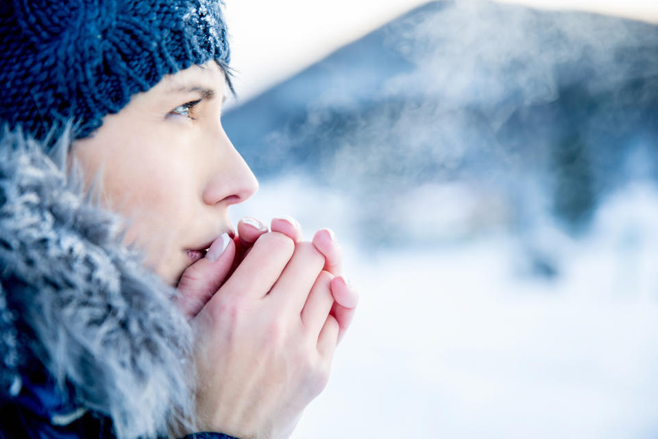 Young woman portrait on a cold winter day. Overcast and cold weather. She is heating her hands with her hot breath.