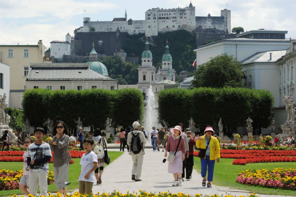 Tourists visit Mirabell Gardens with Fortress Hohensalzburg in the background.