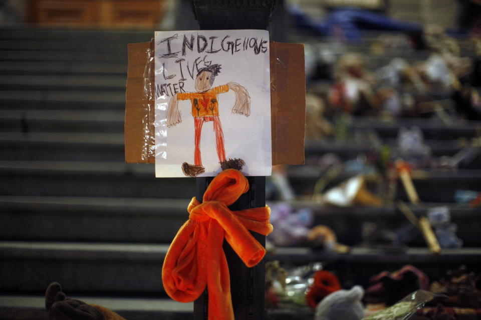 A sign reading "Indigenous Lives Matter" is taped to a lamp post in front of a memorial to the victims of Canada's residential school system made up of shoes, teddy bears, orange shirts and other tributes placed on the steps outside the legislature, in Victoria, Thursday, July 1, 2021. (Chad Hipolito/The Canadian Press via AP)