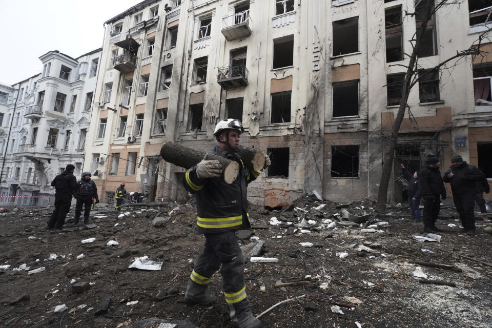 An emergency worker carries pieces of a sawn tree in front of a residential building which was hit by a Russian rocket at the city center of Kharkiv, Ukraine, Sunday, Feb. 5, 2023. (AP Photo/Andrii Marienko)