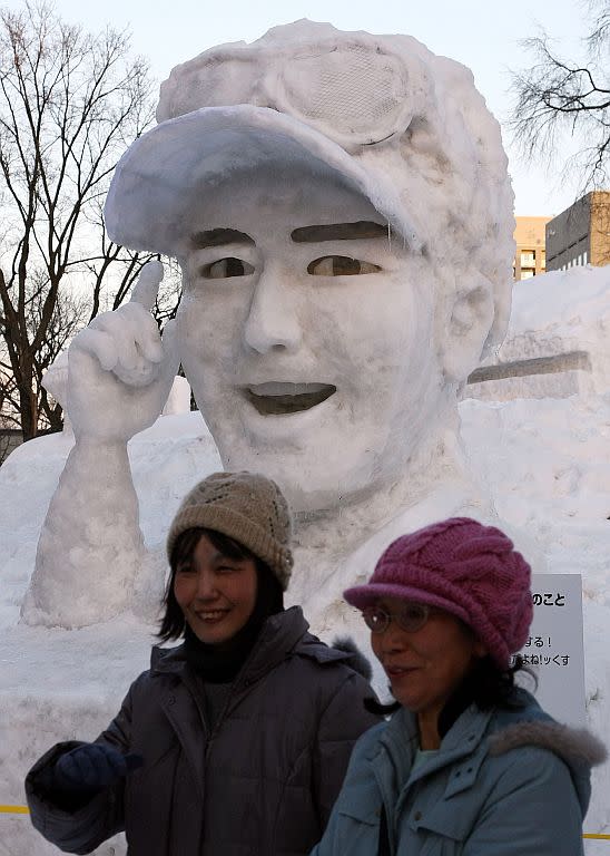Women walk by an ice sculpture of Japanese golfer Ryo Ishikawa ahead of the opening of the 60th Sapporo Snow Festival in Sapporo, Japan.