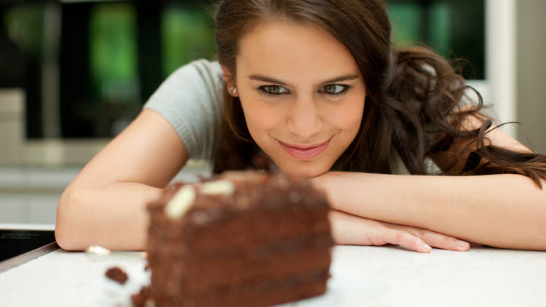 A woman smiling at a piece of chocolate cake