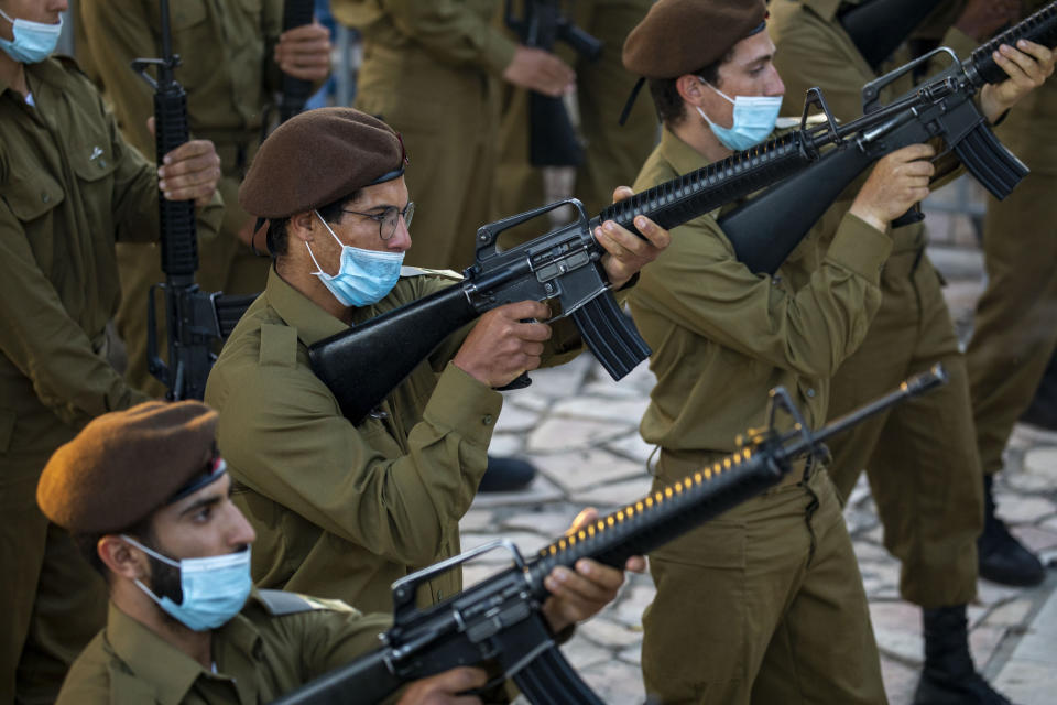 Israeli soldiers wearing face masks to protect against the spread of the coronavirus fire in honor of Israeli army Staff Sgt. Amit Ben-Yigal during his funeral in Beer Yaakov, Israel, Tuesday, May 12, 2020. Ben Ygal, 21, was killed early Tuesday during a West Bank arrest raid when a rock thrown off a rooftop struck him in the head, the military said, capping a surge in violence ahead of a visit to the region by the U.S. secretary of state. (AP Photo/Ariel Schalit)