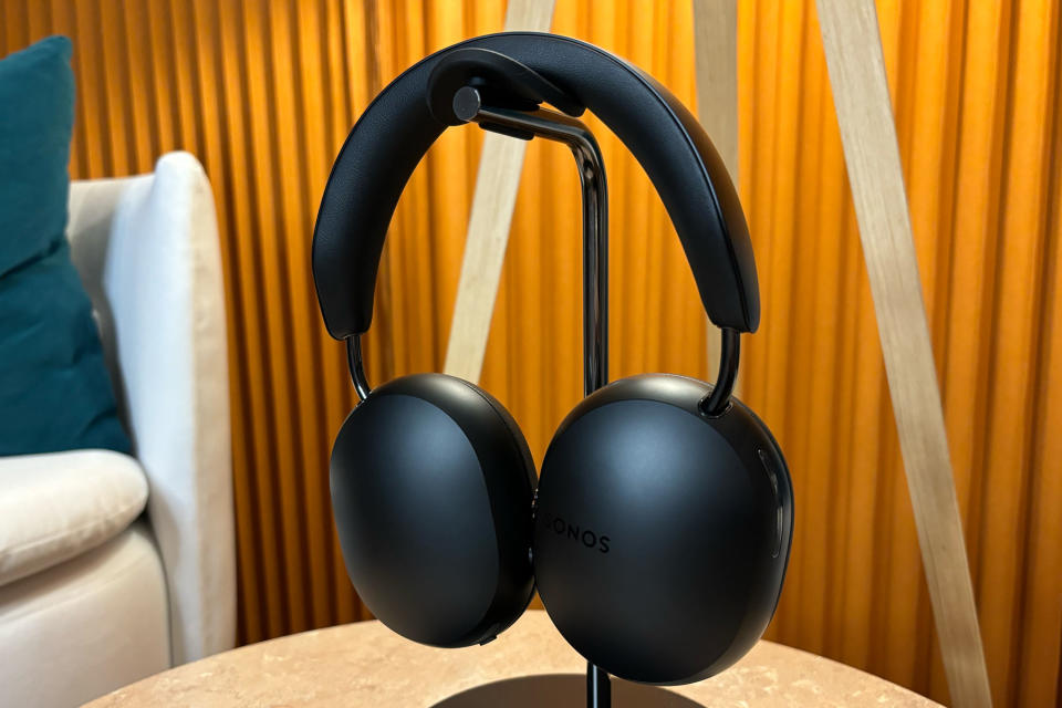 <p>Black headphones on stand sitting on a small table, ear cups rotated to show the outside panel.</p>

