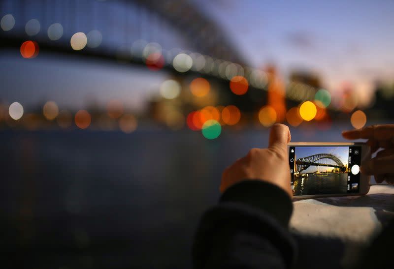 FILE PHOTO: A tourist takes a photograph on their iPhone of the Sydney Harbour Bridge at sunset on a spring day in central Sydney