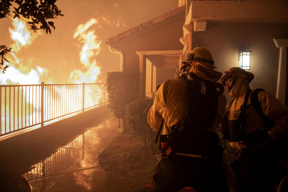 In this Thursday, Oct. 10, 2019 photo, firefighters work on a hose nozzle as the Saddleridge fire burns nears homes in Sylmar, Calif. (Photo: Michael Owen Baker/AP)