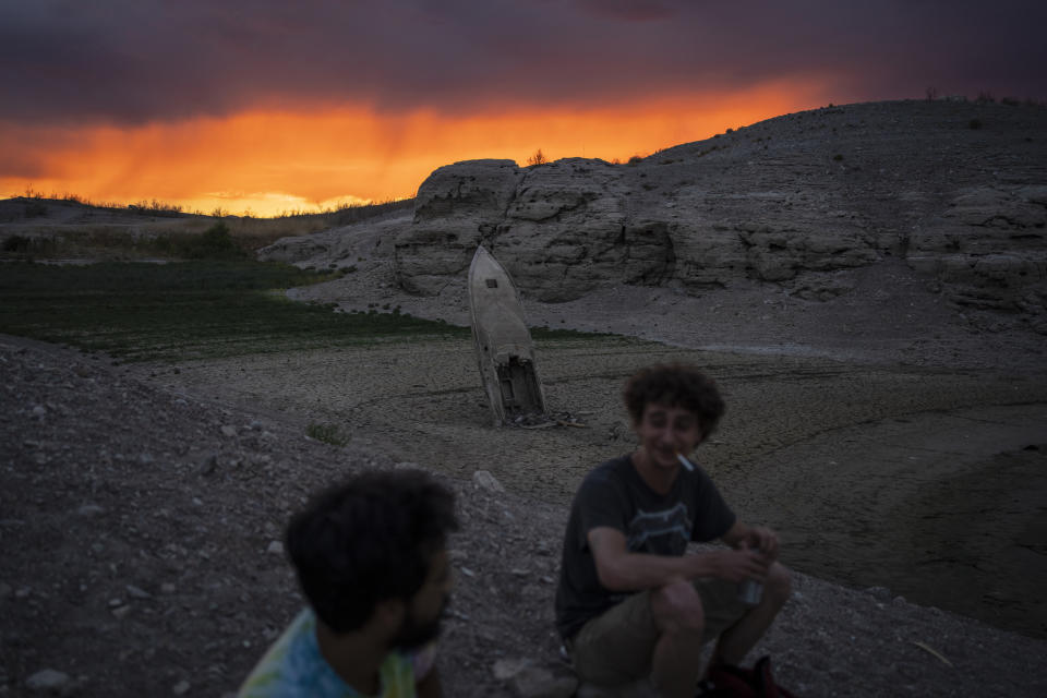 Bobby Rhinebolt (der) y Víctor Pérez conversan en el lecho seco del lago Mead, en Nevada, cerca de Boulder City, el 22 de junio del 2022. Detrás de ellos se ve la punta de un bote semienterrado que se había hundido y quedó al descubierto al bajar el nivel de las aguas. (AP Photo/John Locher)