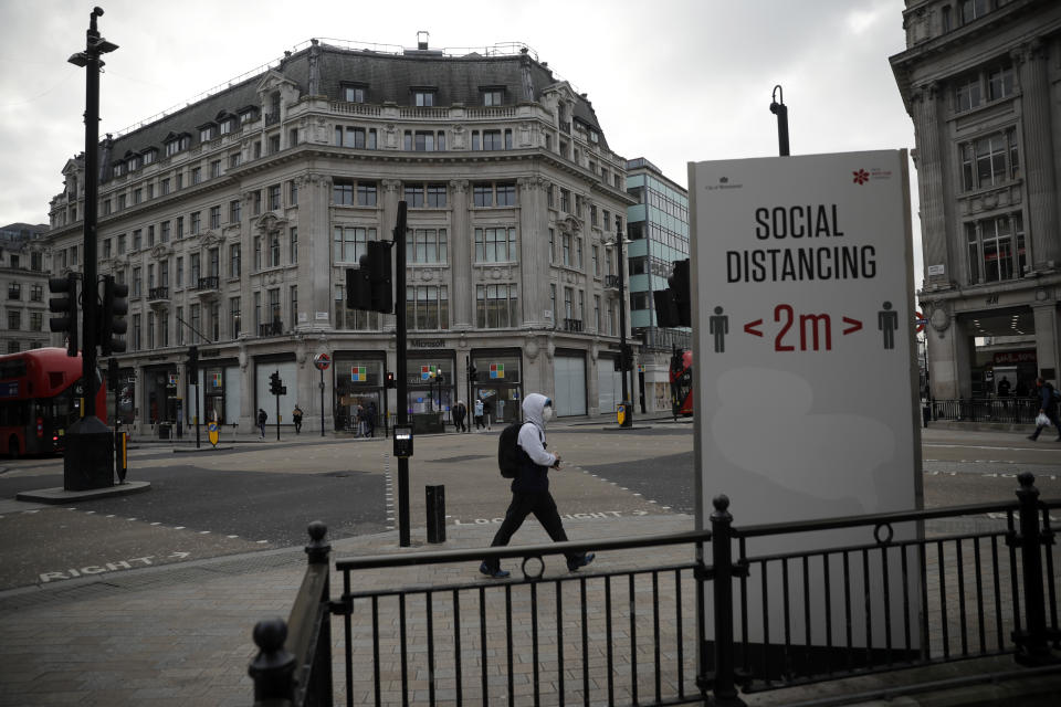 A man wearing a face mask to curb the spread of coronavirus walks past a social distancing sign at Oxford Circus in London, Friday, Jan. 15, 2021, during England's third national lockdown since the coronavirus outbreak began. The U.K. is under an indefinite national lockdown to curb the spread of the new variant, with nonessential shops, gyms and hairdressers closed, most people working from home and schools largely offering remote learning. (AP Photo/Matt Dunham)