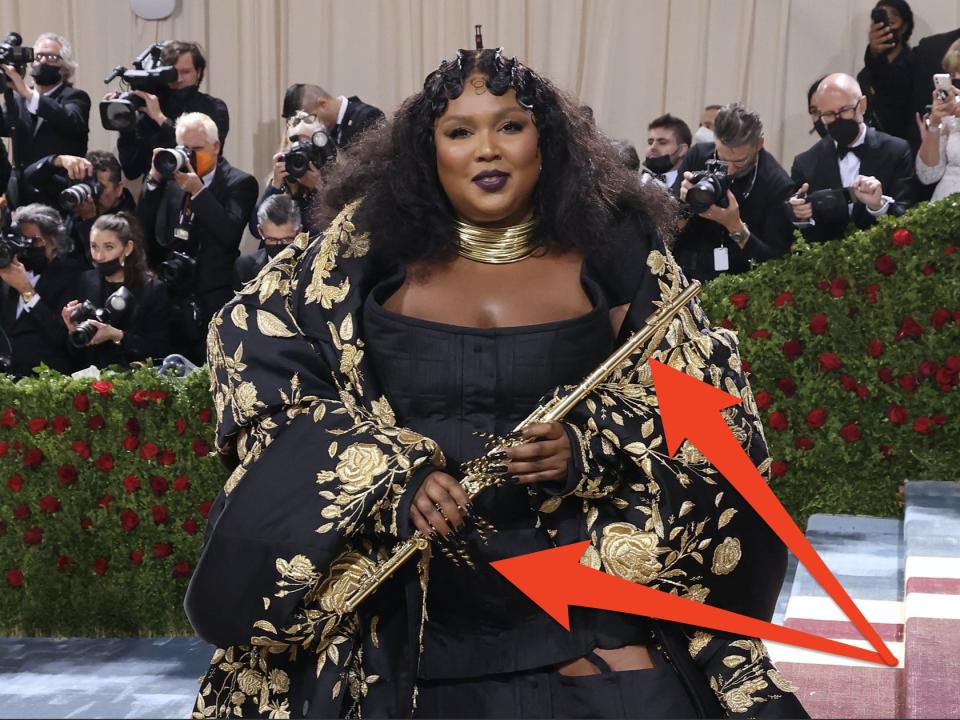 Lizzo in black and gold met gala dress with long nails and flute