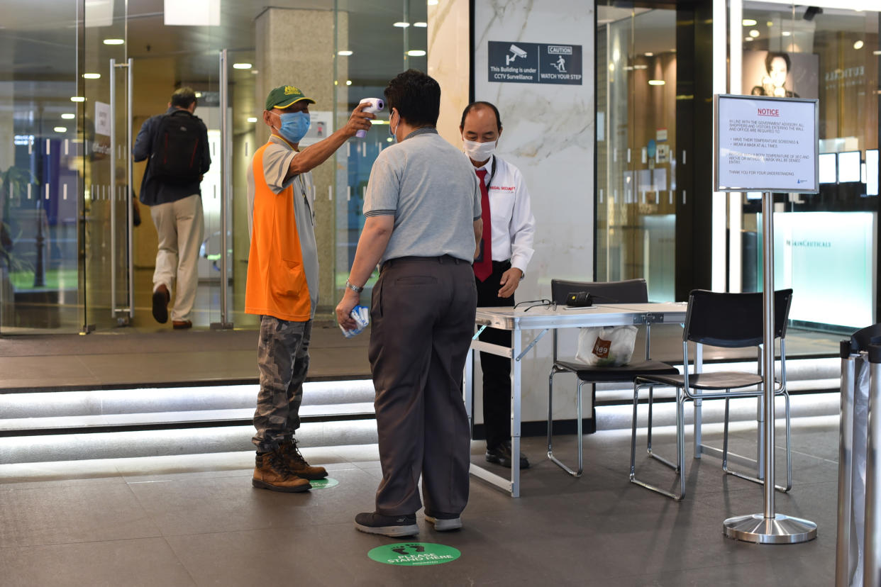 A man wearing a face mask uses a thermal scanner to check on the temperature of an individual before he can enter a building in Singapore Tuesday, June 2, 2020. Singapore reopened 75 percent of its economy Tuesday, as part of a three-phase controlled approach to end a virus lockdown since early April. (AP Photo/YK Chan)