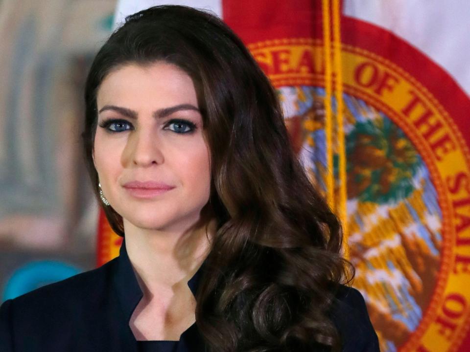 Casey DeSantis stands in front of the flag of Florida with a serious expression