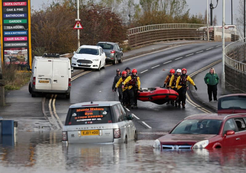 Rescuers carry an inflatable raft as the cars sit in floodwater in Rotherham