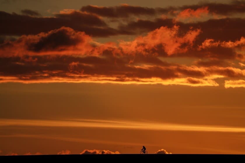 The setting sun lights the sky as a cyclists peddles around the Santa Fe Dam Recreational Area.