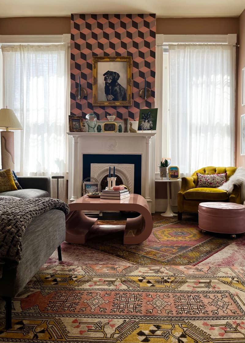 View of pink living room with white mantel, graphic wallpaper, and multiple patterned area rugs.