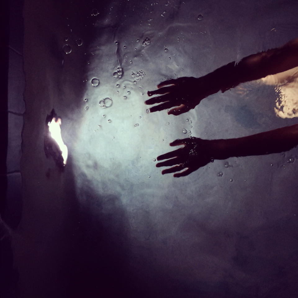 Hands reaching out underwater towards a light source