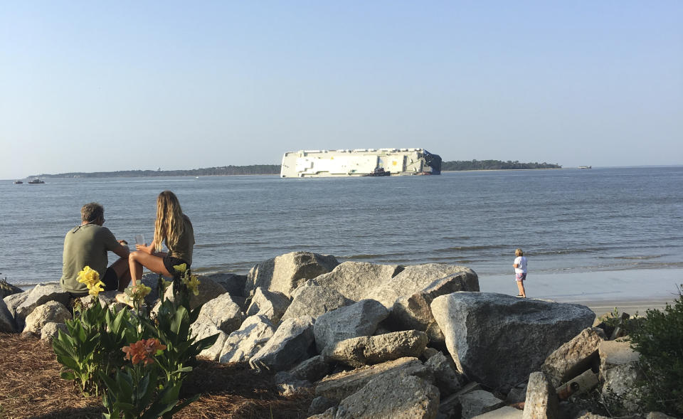 In this photo provided by Tara Jones, people look at a capsized cargo ship near a port on the Georgia coast, Sunday, Sept. 8, 2019. Rescuers were searching Sunday for multiple crew members of the ship that overturned and caught fire in St. Simons Sound, Ga. (Tara Jones via AP)