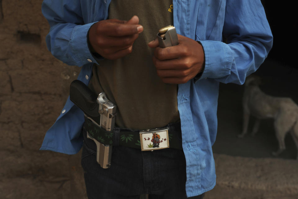 Luis Gustavo Morales loads a bullet into a clip at his home in Ayahualtempa, Guerrero state, Mexico, Wednesday, April 28, 2021. The 15-year-old, who says he always carries the pistol, is the only boy who joins his father every 16 days for shifts to guard their town's entrance. (AP Photo/Marco Ugarte)