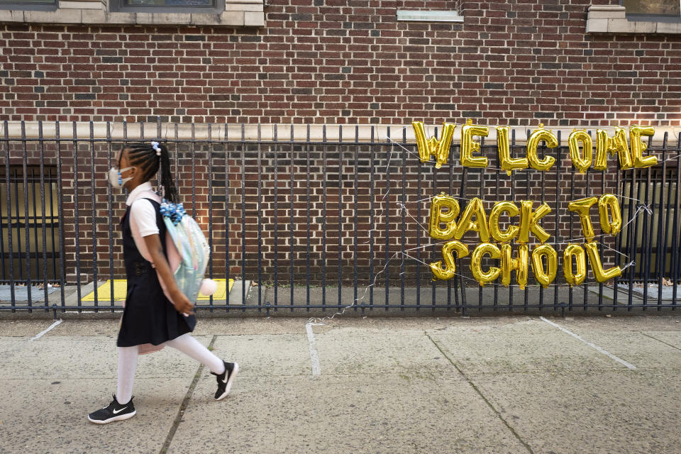 FILE - In this Sept. 13, 2021, file photo, a girl passes a "Welcome Back to School" sign as she arrives for the first day of class at Brooklyn's PS 245 elementary school in New York. COVID-19 deaths and cases in the U.S. have climbed back to where they were over the winter, fueled by children now back in their classrooms, loose mask restrictions and low vaccination levels. (AP Photo/Mark Lennihan, File)