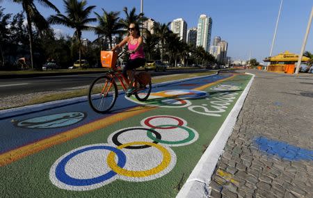 A woman rides her bicycle as she passes over a painting of the Olympic rings ahead of the Rio 2016 Olympic games near Barra da Tijuca beach in Rio de Janeiro, Brazil, July 27, 2016. REUTERS/Sergio Moraes