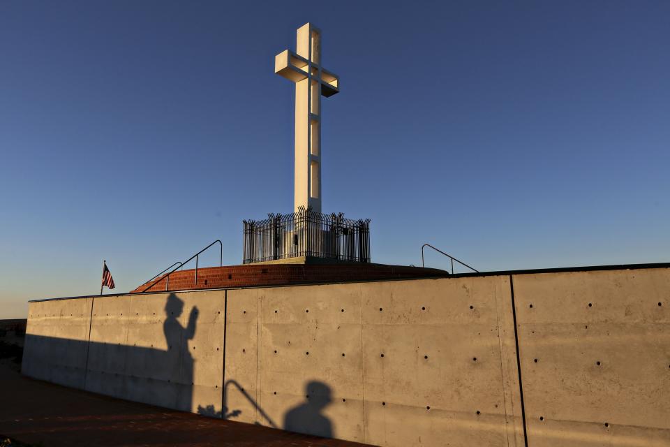 People are silhouetted against a wall as they photograph the massive cross sitting atop the Mt. Soledad War Memorial in La Jolla