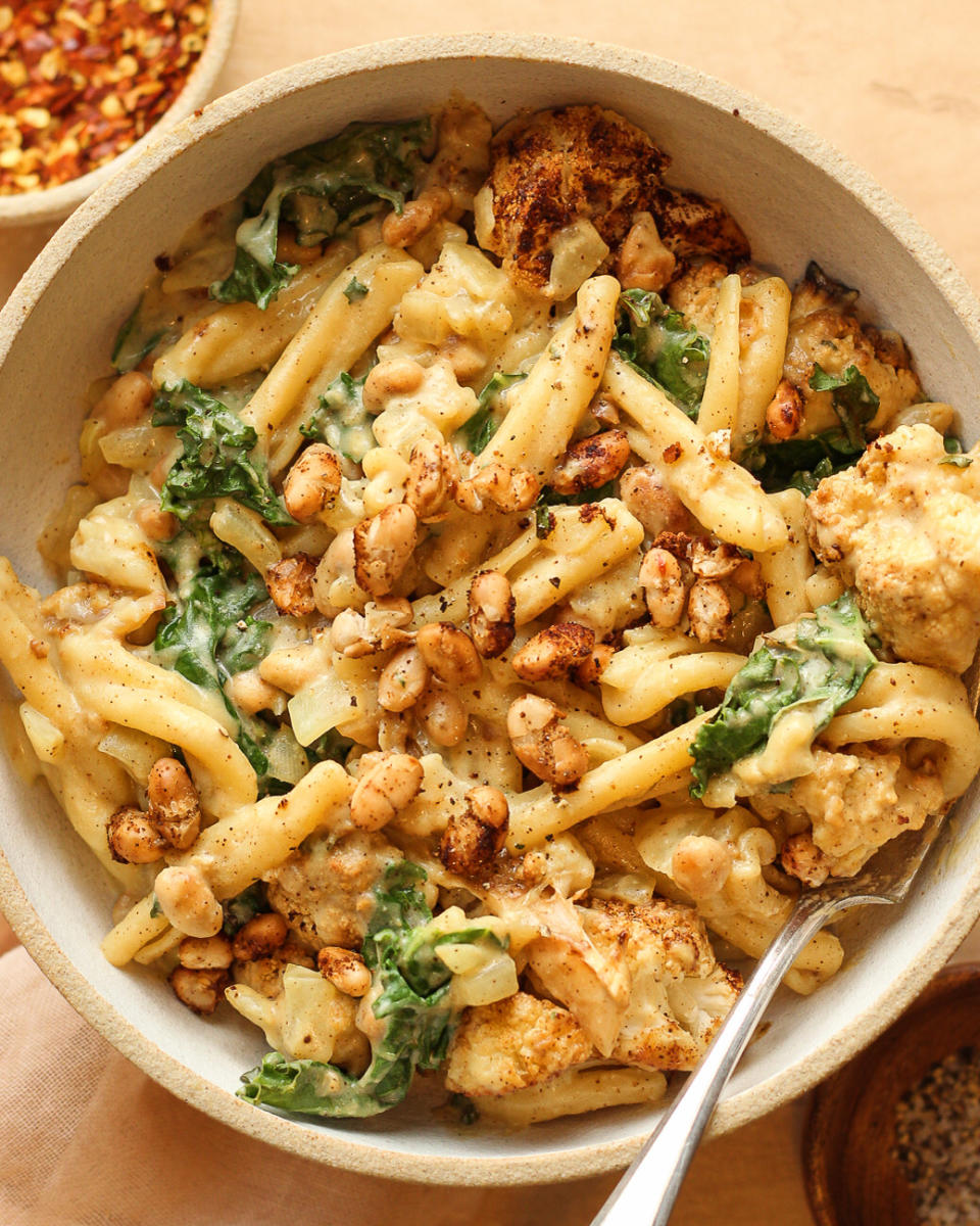 Bowl of mac and cheese with roasted cauliflower and greens, topped with toasted breadcrumbs