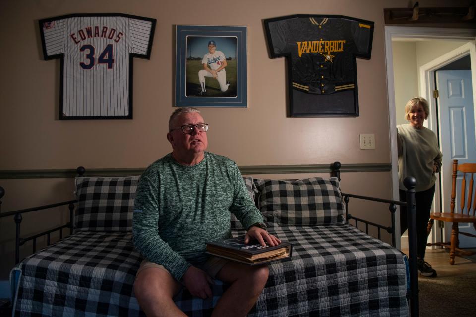 Jeff Edwards, holds a photo album of old newspaper clippings and other items from when he played baseball, as his wife looks in at him at his home in Mt. Juliet, Tenn., Thursday, March 28, 2024.