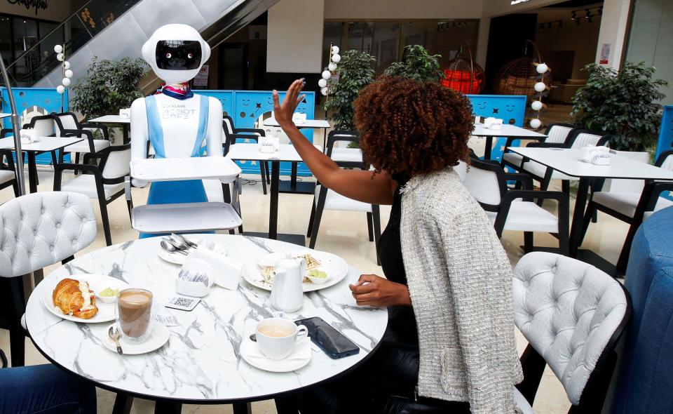 Caroline Nyaga waves and says thank you to the robot waitress that has brought food to her dining table. 