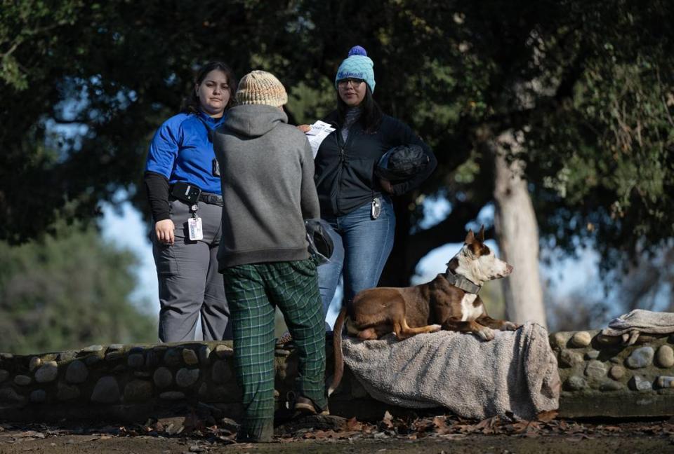 Community Health and Assistance Team (CHAT) outreach specialist Megan Dill, left, and BHRS housing specialist Asuzena Pena, right, talk with a homeless man in Tuolumne River Regional Park during Stanislaus County’s 2024 Point-in-Time count of unsheltered homeless people in Modesto, Calif., Thursday, Jan. 25, 2024.
