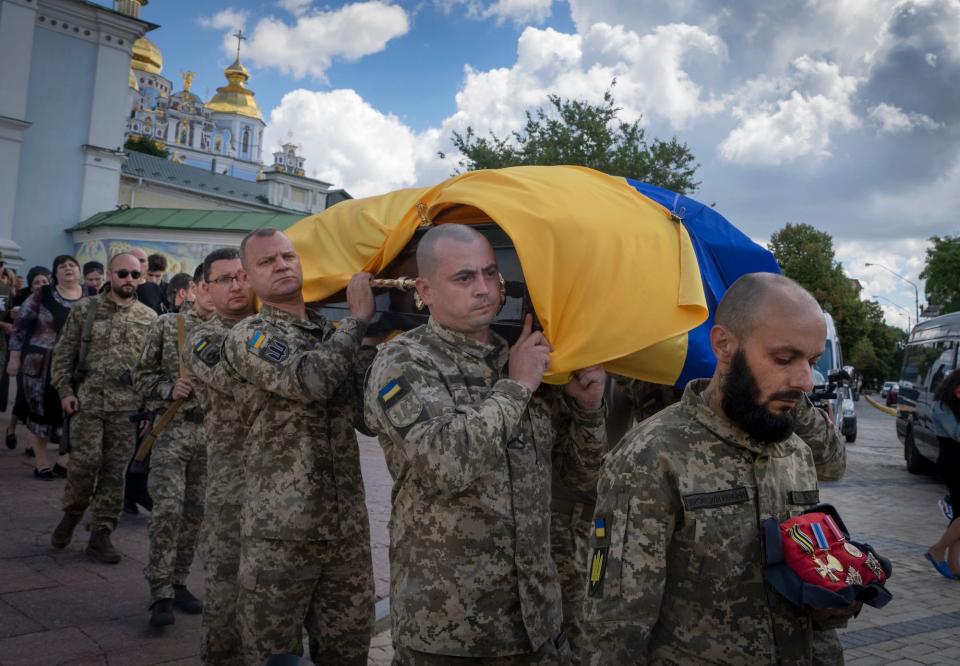 Ukrainians soldiers in camouflage gear carry a coffin wrapped in a Ukrainian flag