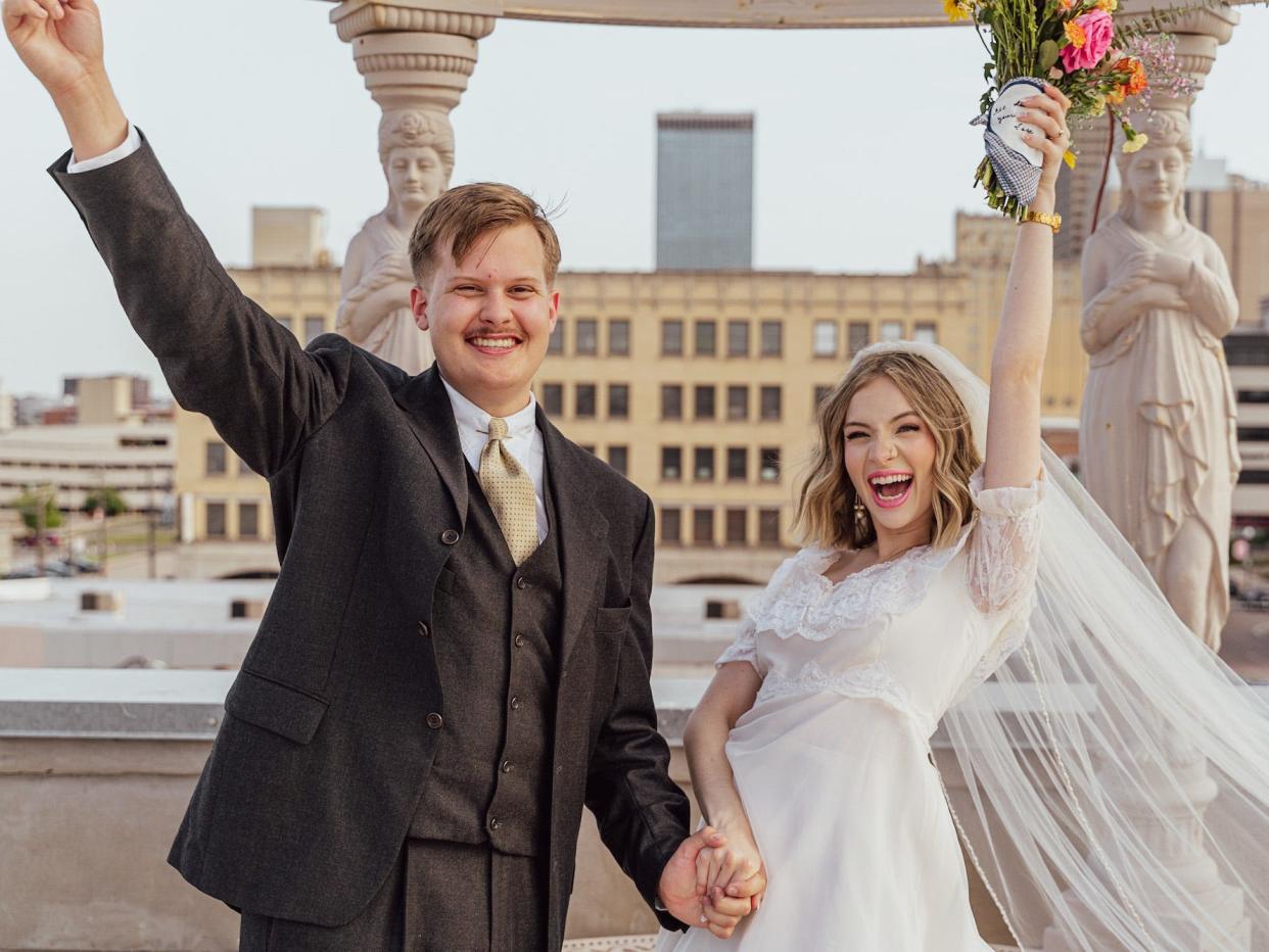 A bride and groom raise their arms in excitement on their wedding day.