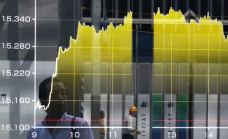 A pedestrian is reflected on an electronic board showing the graph of the recent fluctuations of Japan's Nikkei average outside a brokerage in Tokyo June 19, 2014. REUTERS/Yuya Shino