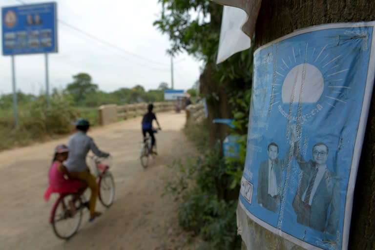 This picture taken on August 16, 2017 shows people cycling past a poster for the Cambodia National Rescue Party (CNRP) showing the images of leader Kem Sokha (2nd R) and former leader Sam Rainsy (R), in a village in Kandal province