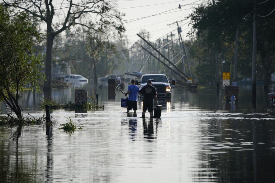 People walk up a street flooded in the aftermath of Hurricane Ida, Wednesday, Sept. 1, 2021, in Jean Lafitte, La. Louisiana residents still reeling from flooding and damage caused by Hurricane Ida are scrambling for food, gas, water and relief from the oppressive heat. (AP Photo/John Locher)