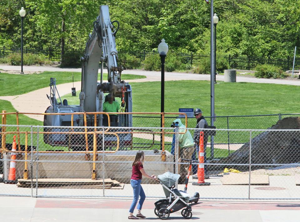 A woman pushes a stroller past construction workers who are installing a chilled water line into the former O'Neil's building at the entrance to Lock 3 in Akron on Tuesday.