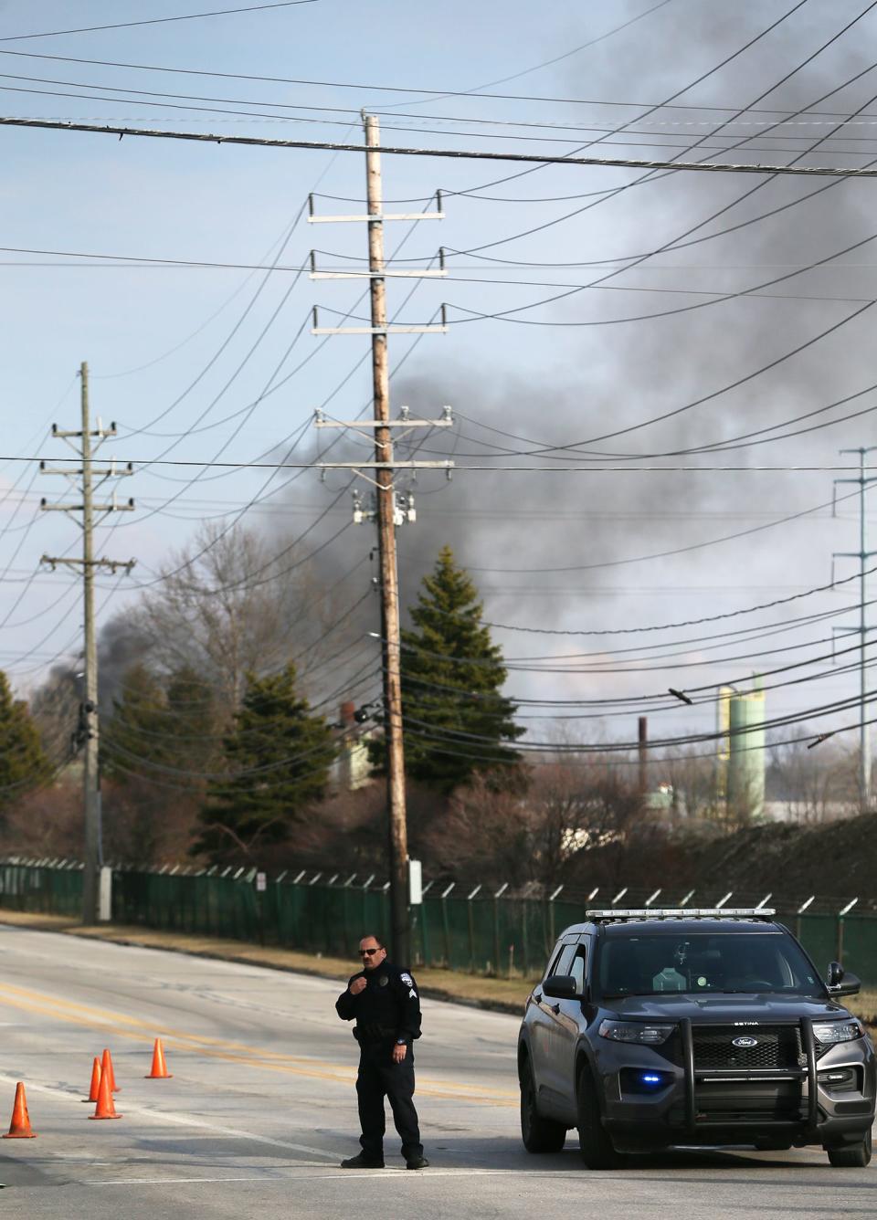 A police officer blocks access to Alexander Road at Northfield Road as smoke billows from a fire at I. Schumann & Co. in Oakwood on Monday. Multiple agencies responded to the fire and explosion at the industrial facility.