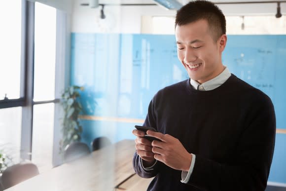 Young Asian man smiling while chatting on mobile device.