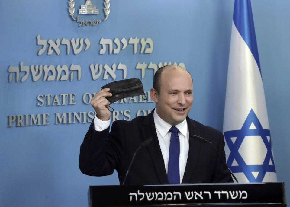 Israeli Prime Minister Naftali Bennett holds up a face mask as he delivers a statement on the coronavirus situation, in Jerusalem Wednesday, July 14, 2021. Bennett said Wednesday that Israel can beat a concerning rise in new coronavirus cases without a nationwide shutdown, but he called on people to wear masks indoors and otherwise comply with safety rules. (AP Photo/Maya Alleruzzo)