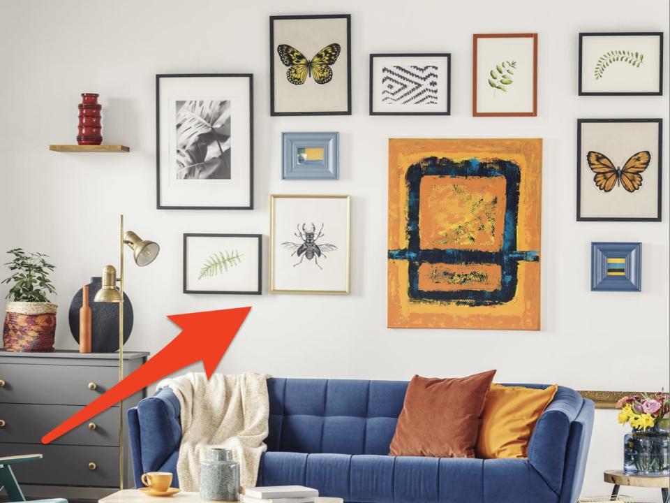 A red arrow pointing to a white wall filled with artwork and framed photos of various sizes