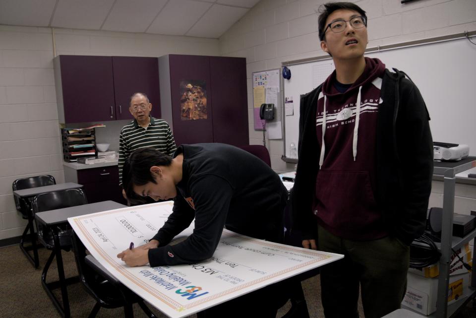 Kevin Guan, center, signs the $10,000 check in Dr. Raymond Eng’s classroom next to Kevin Liu, right, on Friday, April 28, 2023 at High Technology High School in Middletown, New Jersey. The check will be placed on Dr. Eng’s classroom walls. 