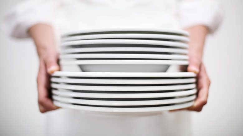 A chef holds a stack of white plates