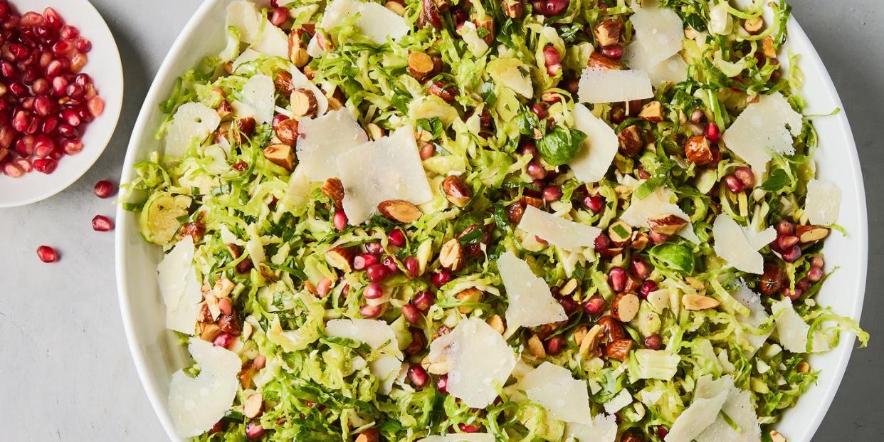 shaved brussels sprouts with pomegranates, shaved parmesan, and chopped toasted almonds in a white bowl