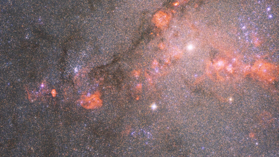     Hubble-Teleskopfoto einer Galaxie voller Sterne und Wolken aus orangerotem Gas. 