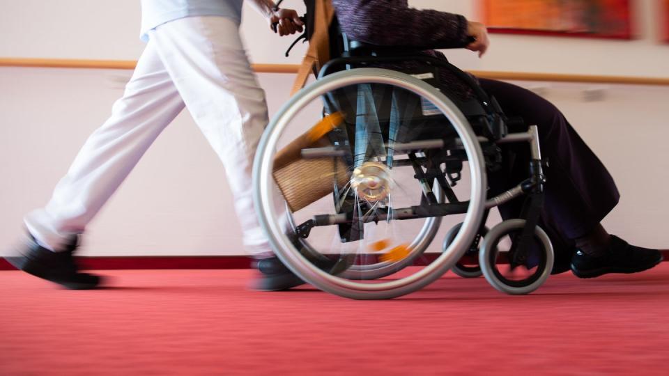 Ein Pfleger schiebt eine Frau in einem Rollstuhl.
