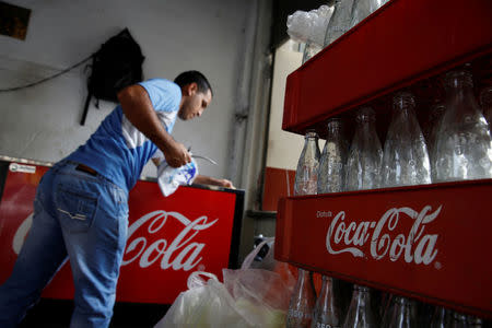 Cases of Coca-Cola with empty bottles are seen next to a man cleaning a fridge with the logo of the company, at a food stall on the street in Caracas, Venezuela May 24, 2016. REUTERS/Carlos Garcia Rawlins