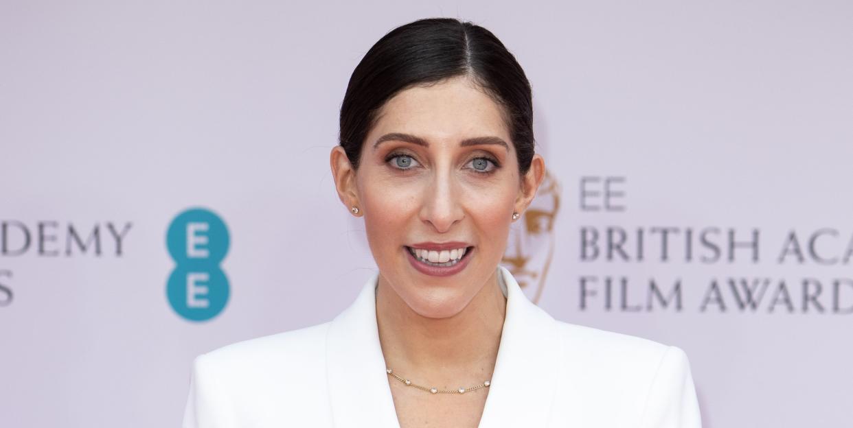 sarah jossel, a woman wearing a white suit with hair up in a bun, smiling at the camera