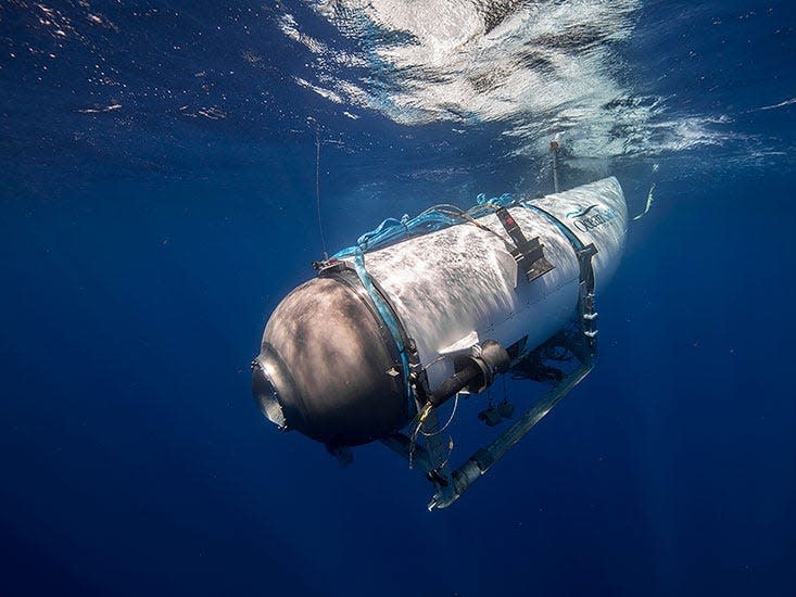 A side view of the Titan submersible, a white cylindrical vessel with a rounded front that has a single porthole, diving into dark blue waters