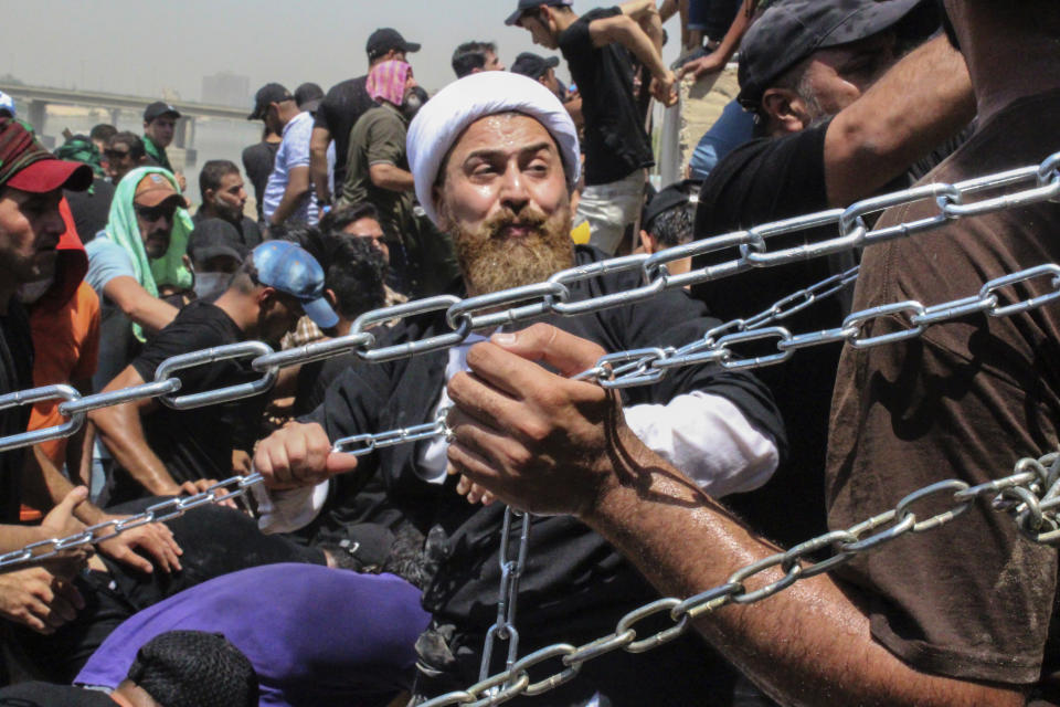 Iraqi protesters use chains to try to remove concrete barriers on their way to the Parliament building in Baghdad, Iraq, Saturday, July 30, 2022 as thousands of followers of an influential Shiite cleric breached the building for the second time in a week to protest the government formation efforts lead by Iran-backed groups.(AP Photo/Adil al-Khazali)