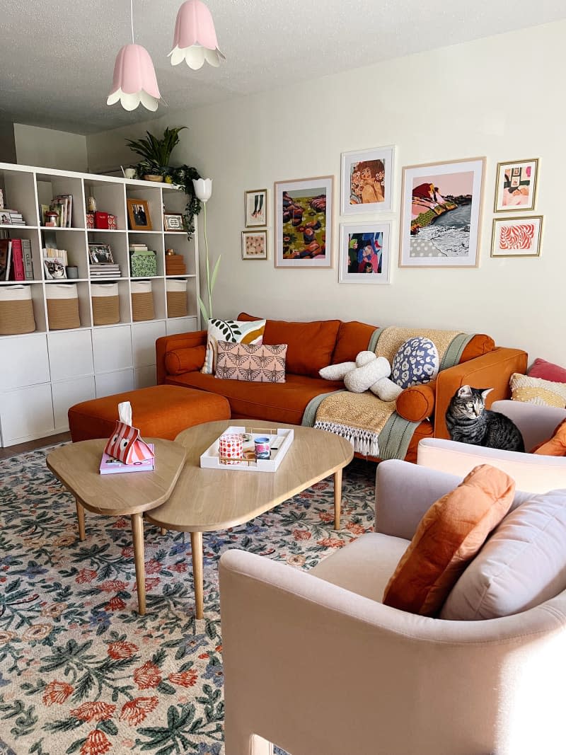 White living room with dark orange sofa, gallery wall and high white shelves