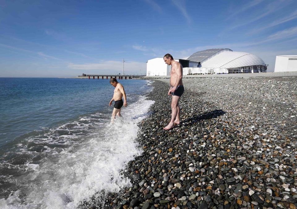 Men wade into the sea on a sunny day as the Olympic Park is seen in the background, during the 2014 Winter Olympic Games in Sochi February 12, 2014. REUTERS/Shamil Zhumatov